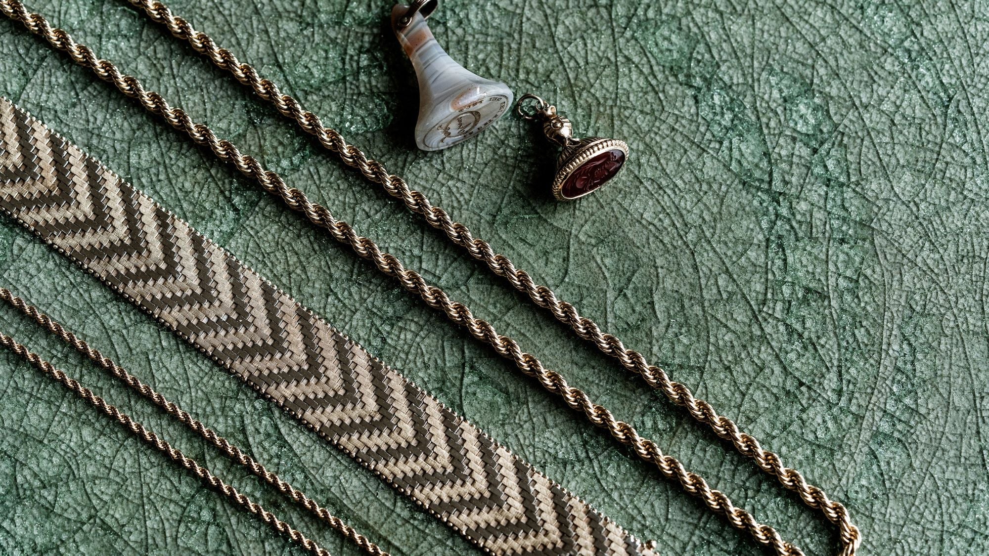 A gold pendant with a large blue-green opal and small clear stones is displayed on rough, dark wood.