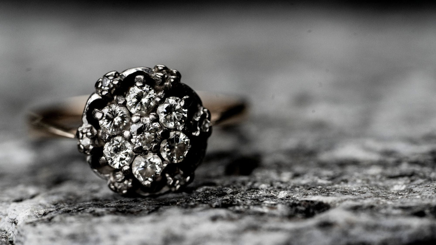A close-up of a diamond cluster ring with several small diamonds set in a circular pattern on a textured gray surface.