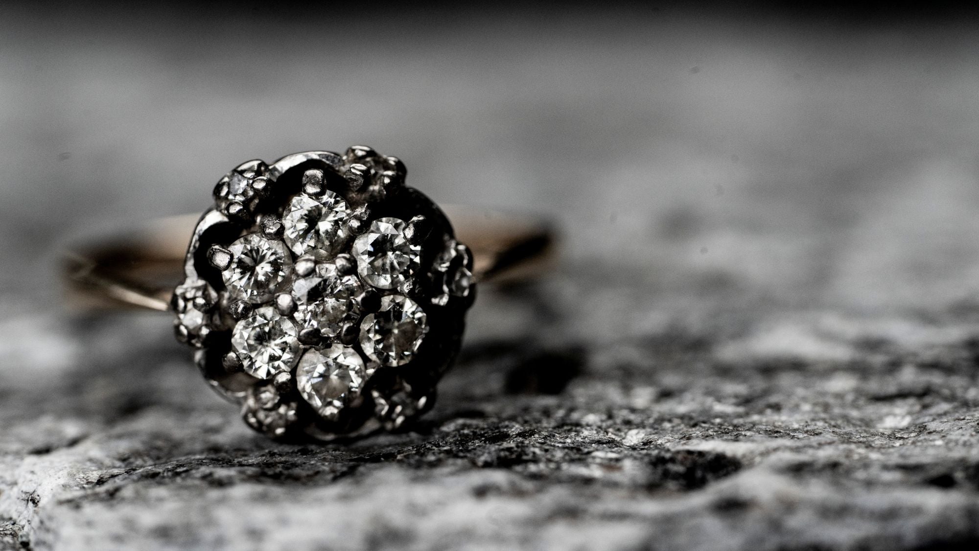 A close-up of a diamond cluster ring with several small diamonds set in a circular pattern on a textured gray surface.