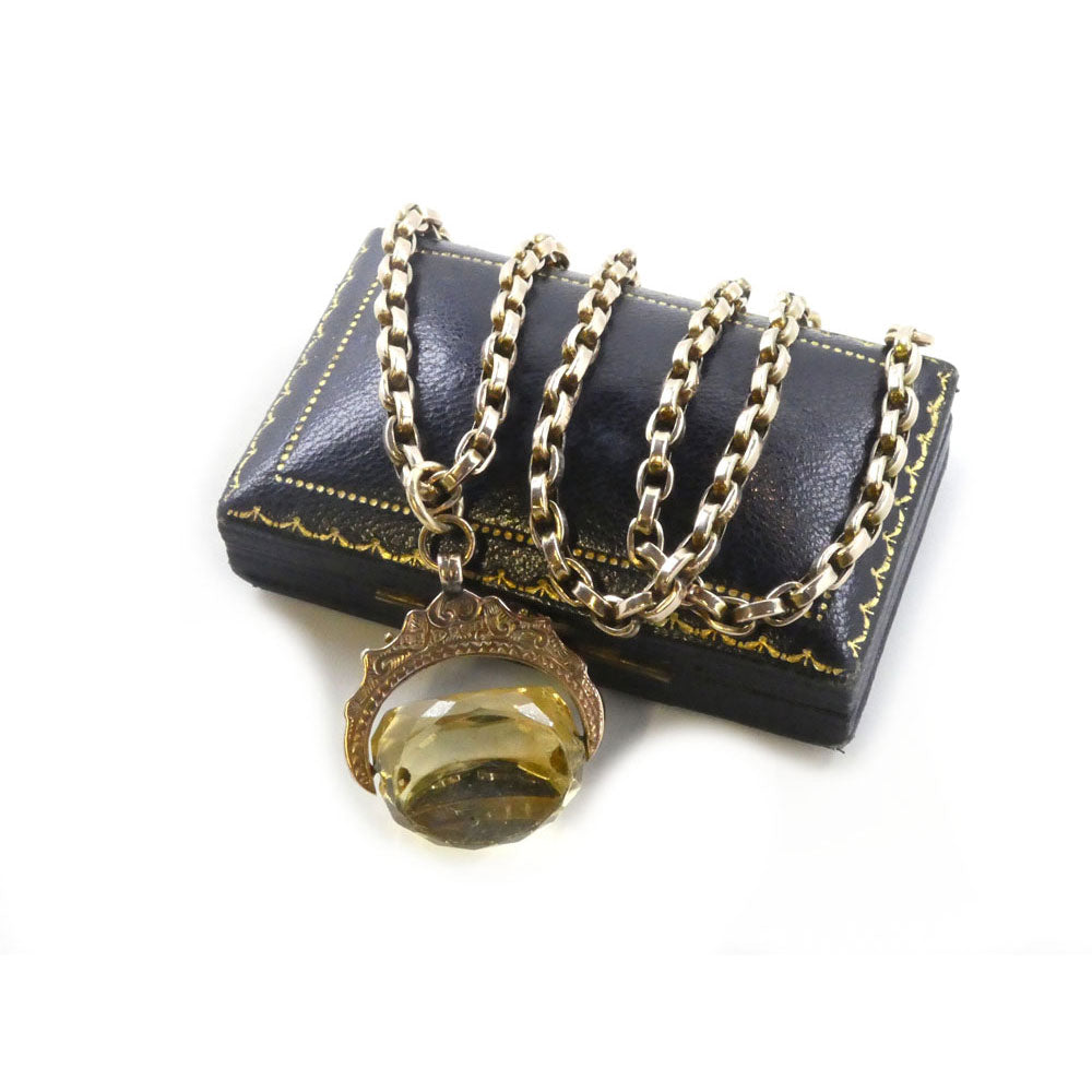 A Victorian Citrine Swivel Pendant and Chain from Hidden Gems rests on a black, rectangular leather box with gold detailing.