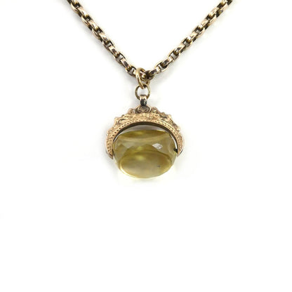 The Victorian Citrine Swivel Pendant and Chain by Hidden Gems is a gold chain necklace with an ornate rose gold pendant featuring a faceted yellow gemstone.